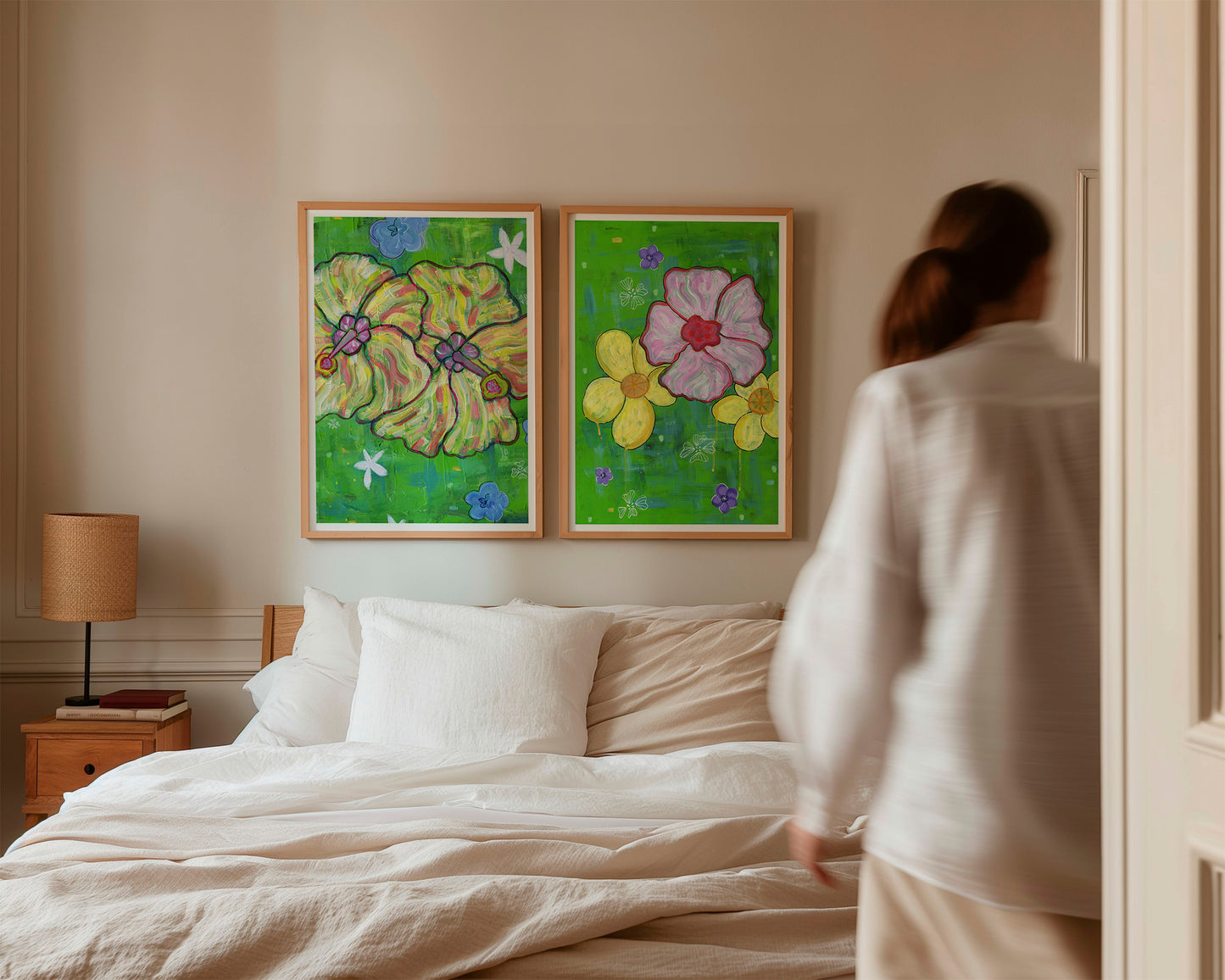 Insitu framed art prints on a bedroom wall hanging above a bed. Print on left contains two bright yellow and pink hue hibiscus flowers. Print on right contains a pink hibiscus flower and two frangipani's. Both prints by MZ LEW ART copyright 2024.